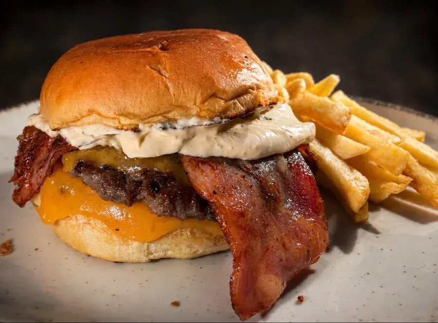 Hamburguesa con queso y tocino, salsa cremosa y papas fritas en un plato.