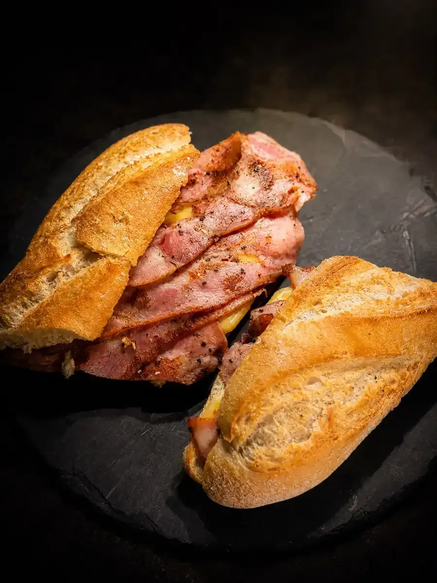 Dos bocadillos de baguette crujiente con carne rosada en rodajas sobre un plato negro.