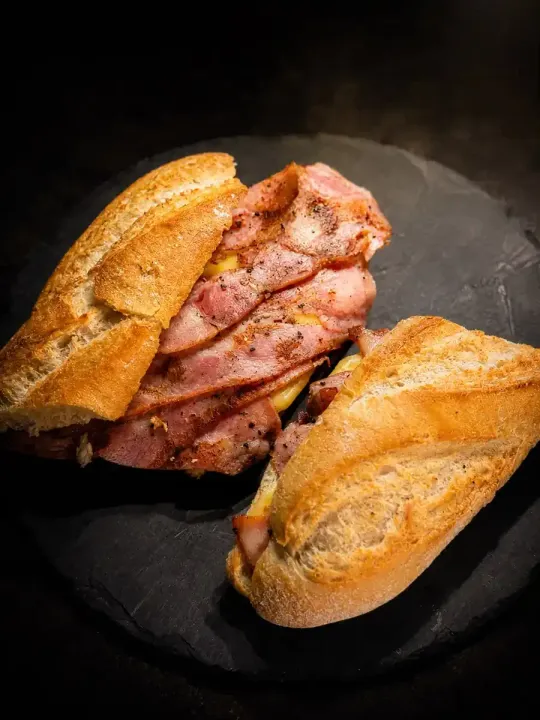 Sándwich de baguette relleno de tocino en un plato negro, con dos mitades de pan crujientes y dorados a su alrededor.