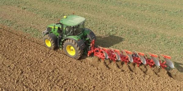 Un tractor verde está arando un campo con un arado rojo acoplado a él.