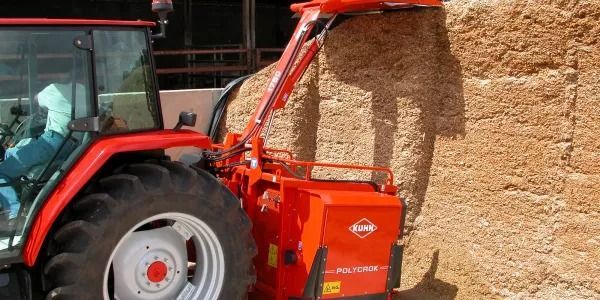 Un tractor rojo circula al lado de una pila de heno.