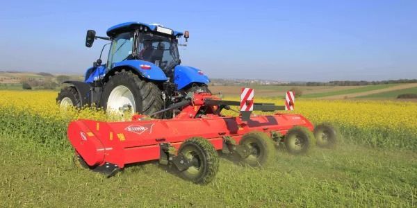 Un tractor azul conduce por un campo de flores amarillas.