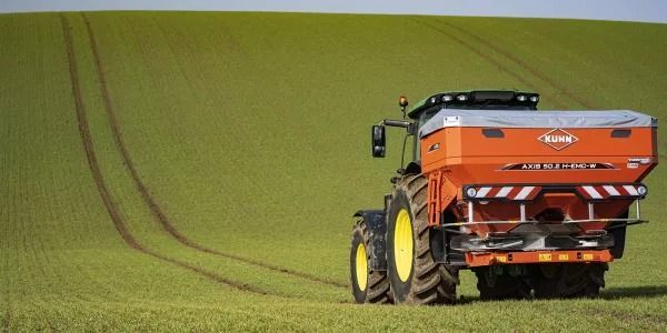 Un tractor está esparciendo fertilizante en un campo verde.