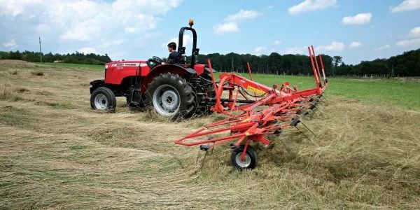 Un tractor rojo circula por un campo de heno.