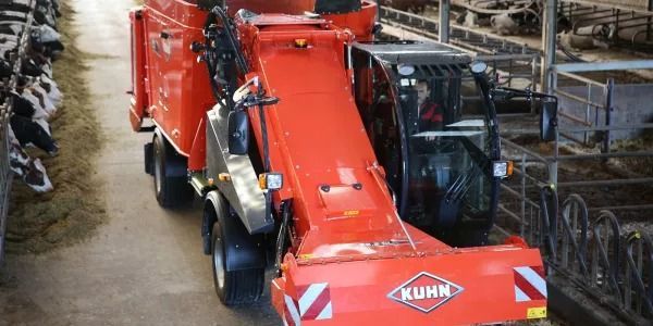 Un tractor rojo circula por una carretera al lado de una hilera de vacas.