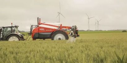 Un tractor está rociando un campo de trigo con un rociador.