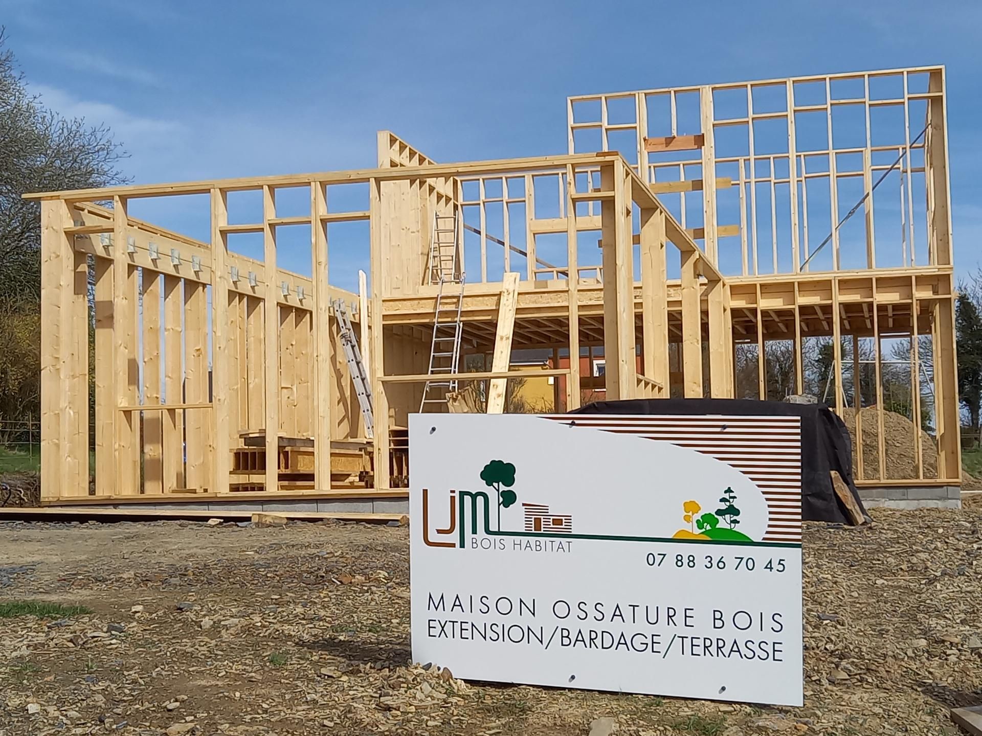 Maison à ossature en bois en construction, charpente apparente et panneau devant, par une journée ensoleillée.