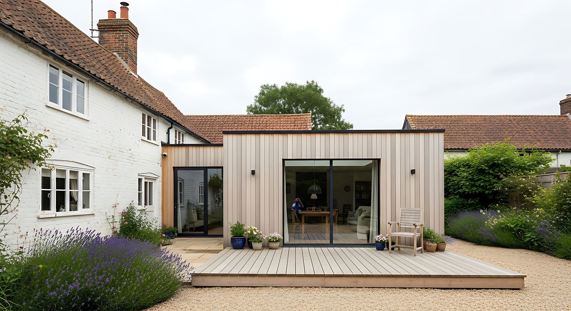 Extension moderne de maison avec portes coulissantes en verre, bardage en bois et patio donnant sur une cour-jardin.