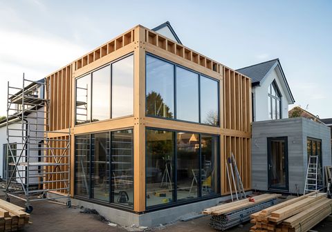 Maison moderne de deux étages en construction, avec de grandes baies vitrées et des échafaudages extérieurs.