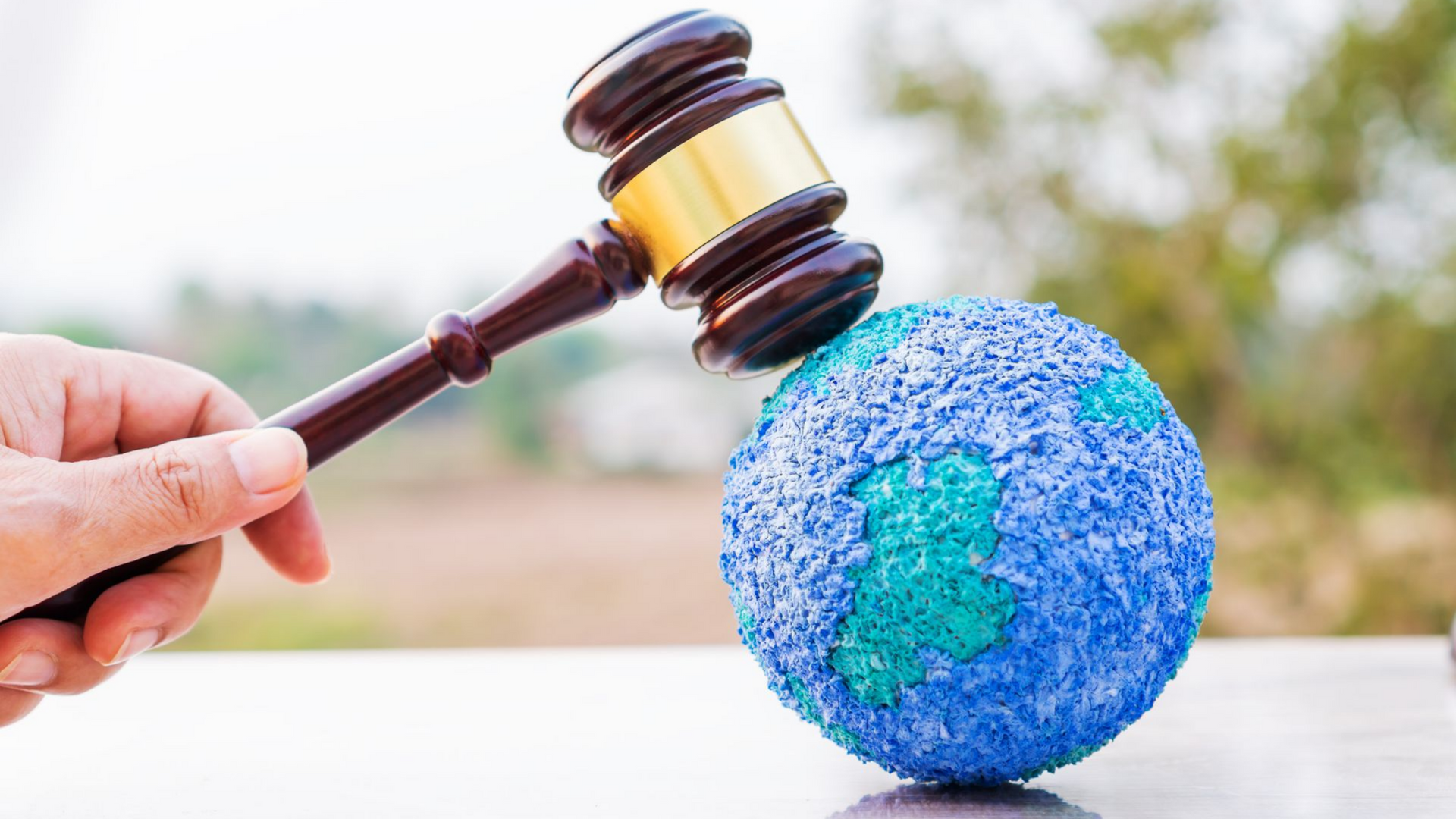 Main tenant un marteau de juge frappant un globe terrestre.