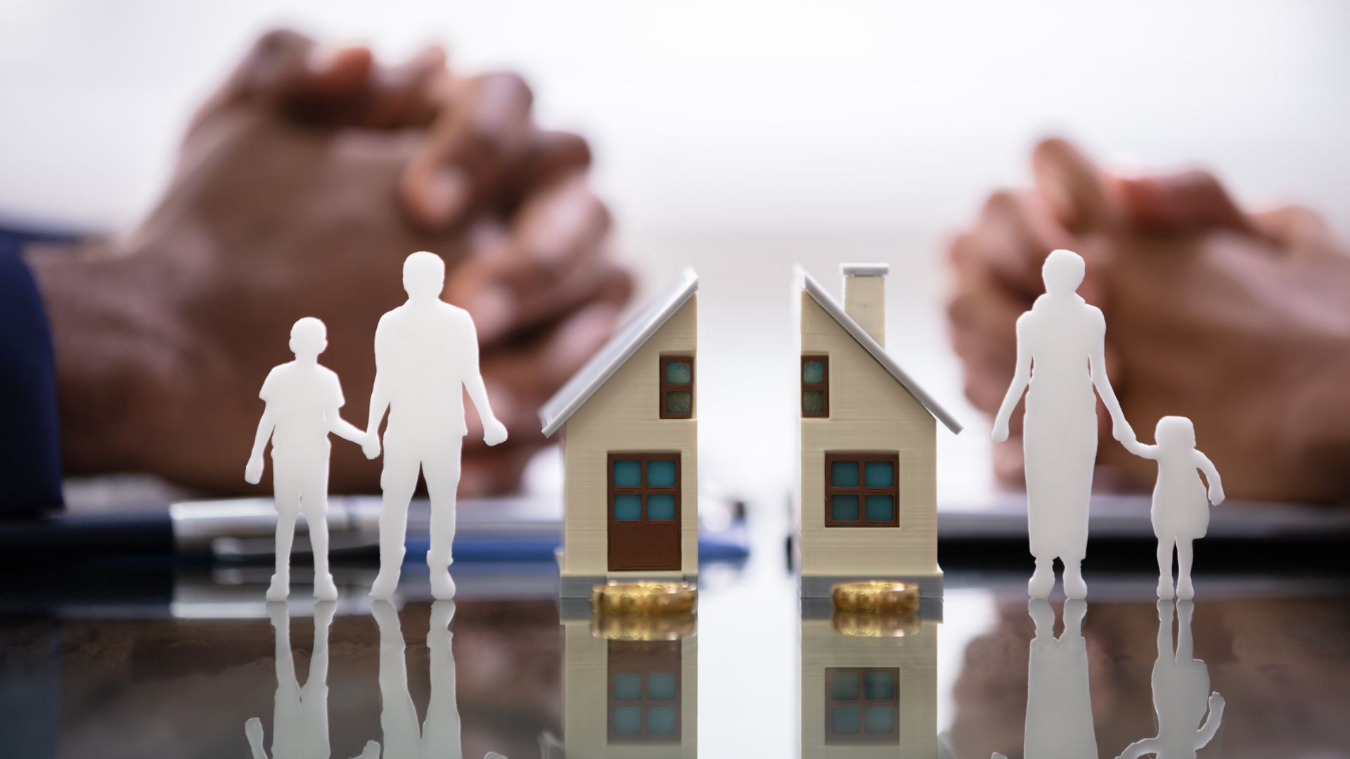 Mains jointes près d'une maquette de maison coupée en deux ; des figurines en papier représentant des membres de la famille de part et d'autre.