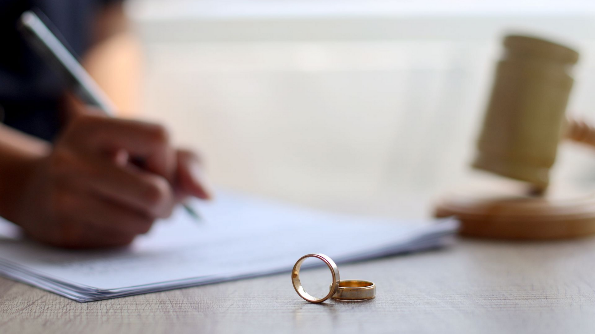 Des alliances sur une table, une personne qui écrit, un maillet en arrière-plan.