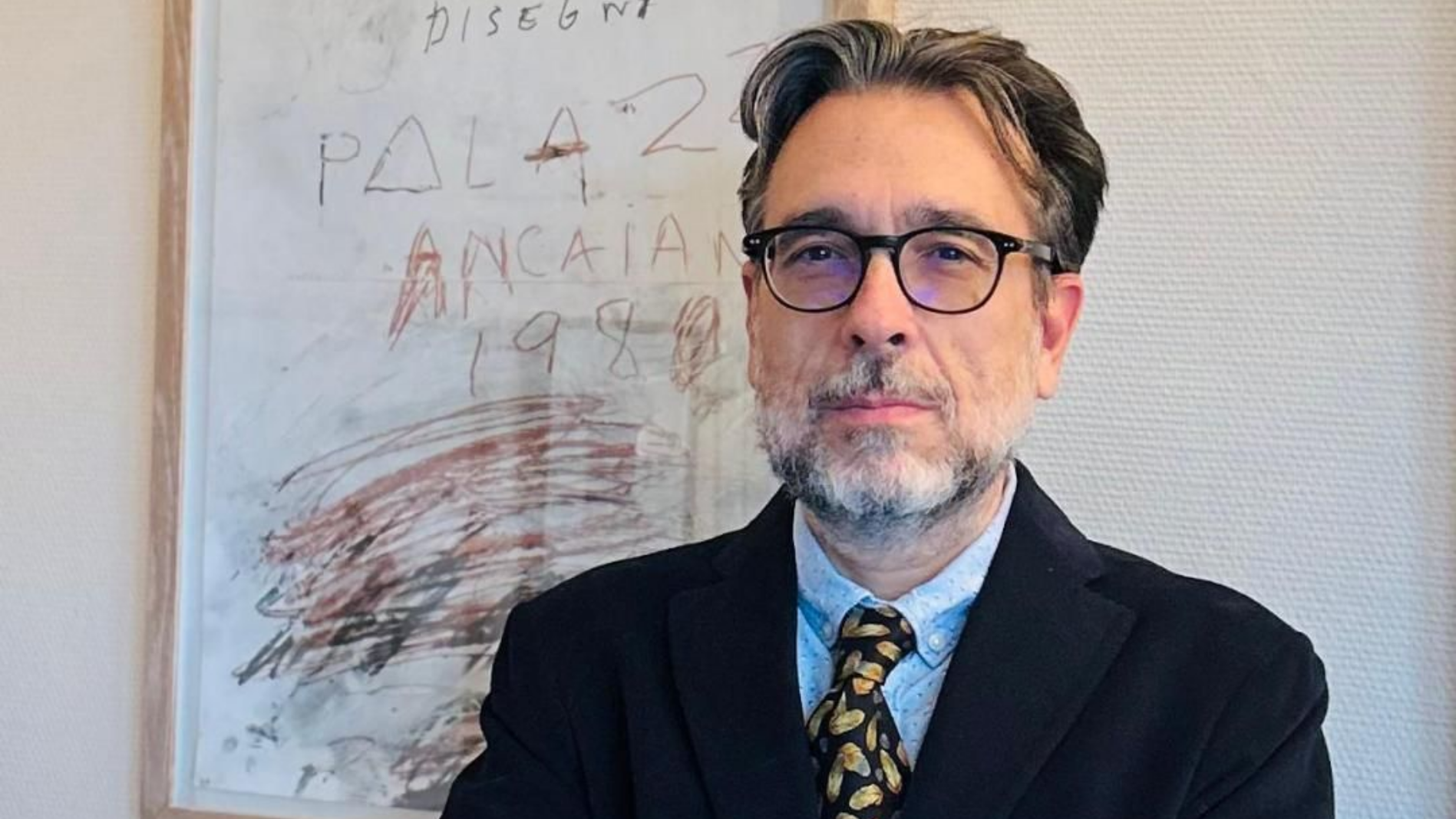 Un homme en costume et lunettes se tient devant un tableau blanc couvert d'écrits et de dessins.