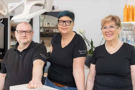 Eine Frau mit blauem und rosa Haar lächelt, während sie ihr Haar im Spiegel betrachtet.