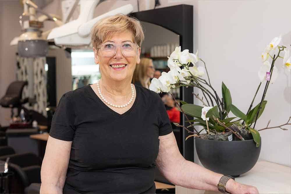 Eine Frau steht in einem Salon neben einer Vase mit Blumen.
