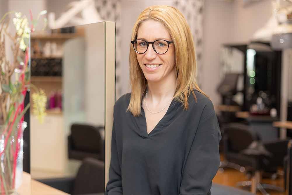 Eine Frau mit Brille steht in einem Salon vor einem Spiegel.