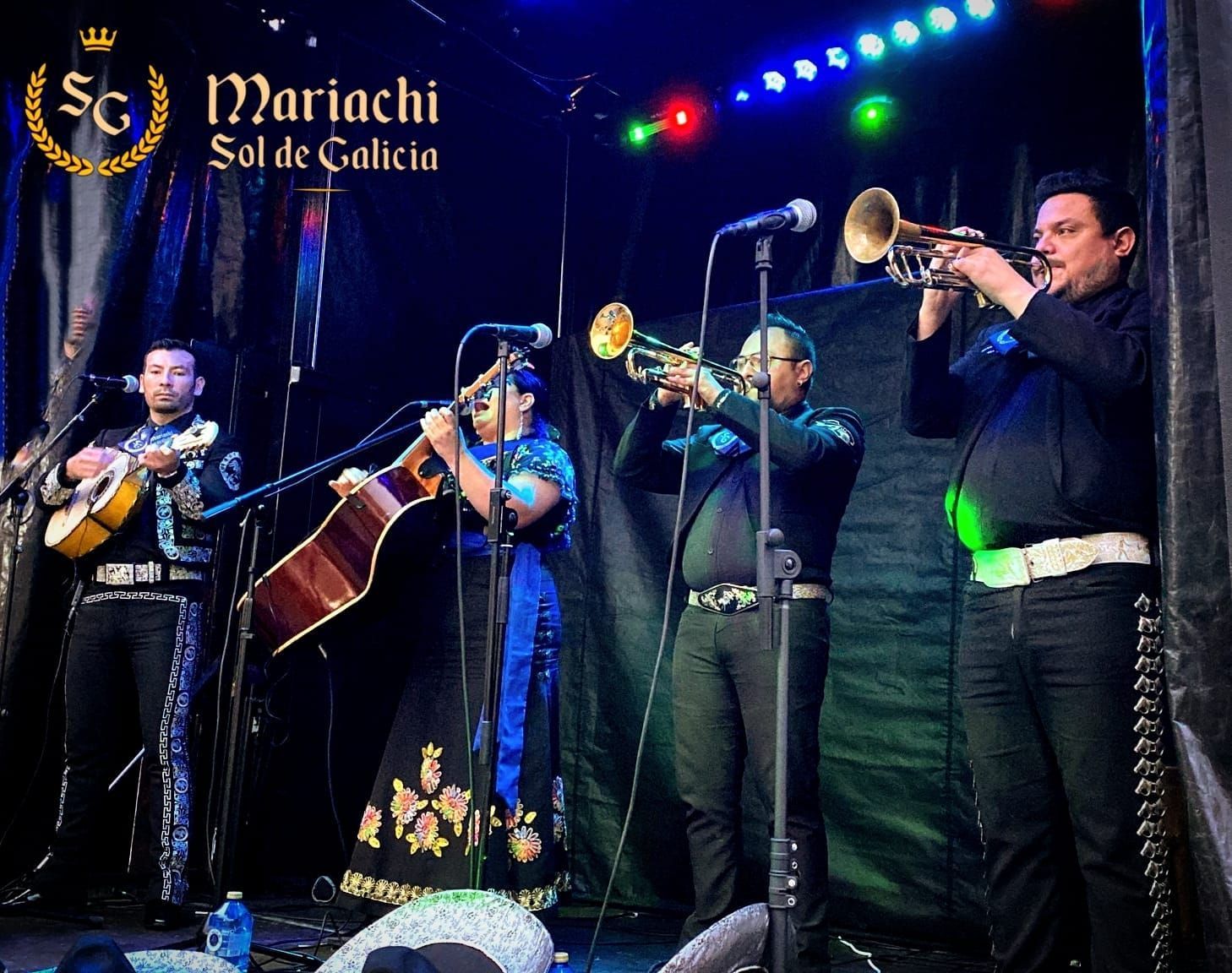 Grupo de mariachis actuando en un escenario oscuro con guitarras, trompeta y luces de colores.