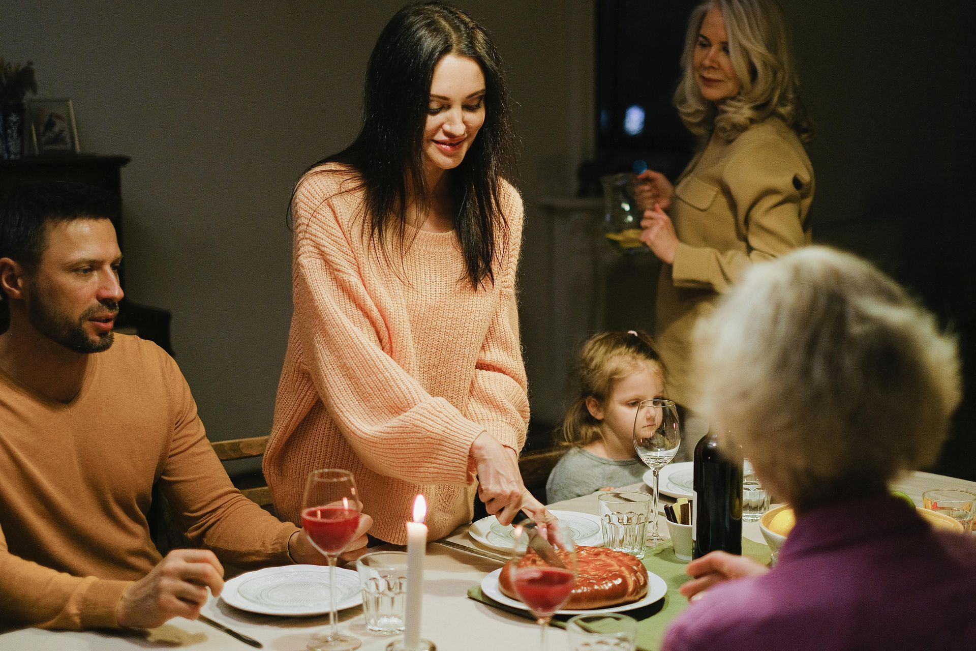 En una casa cálidamente iluminada, la gente se reunía alrededor de una mesa para cenar, servir la comida y charlar.
