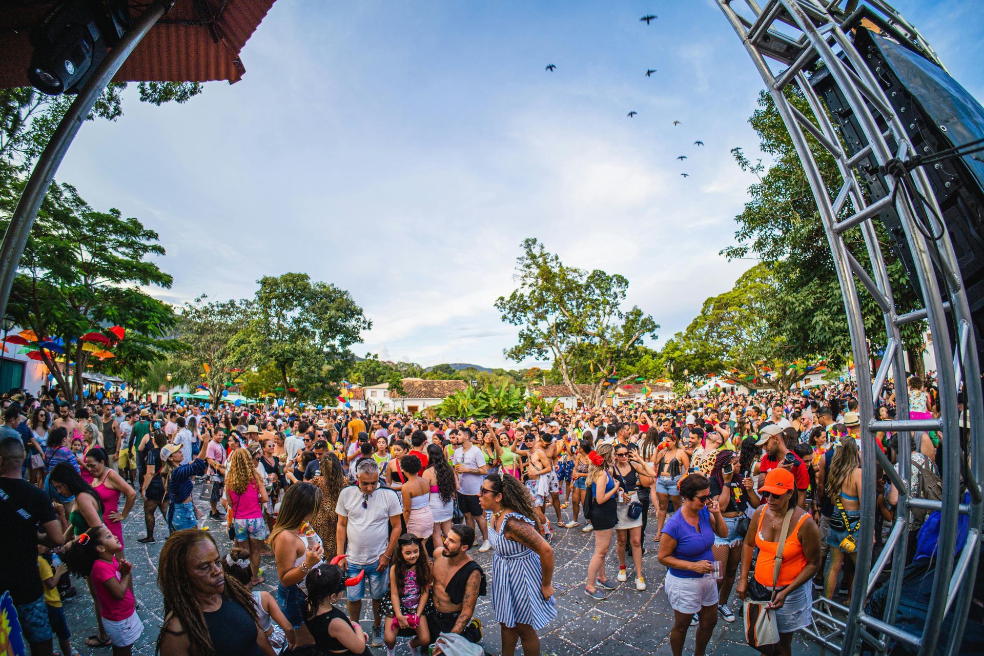 Festival de música al aire libre abarrotado de gente bailando bajo un arco de escenario a plena luz del día.
