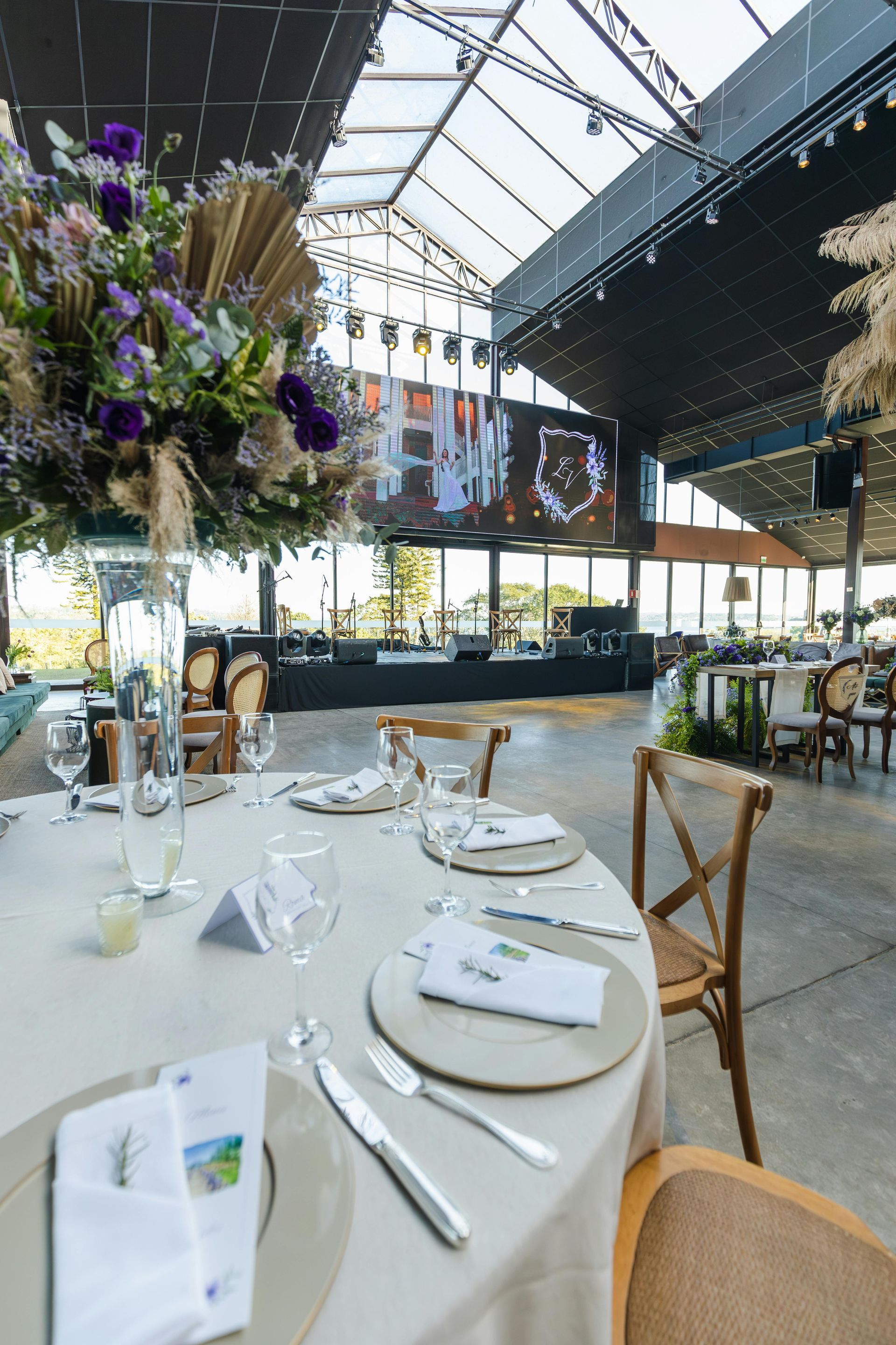 Elegante mesa de banquete en un luminoso espacio con techo de cristal, decoraciones florales colgantes 