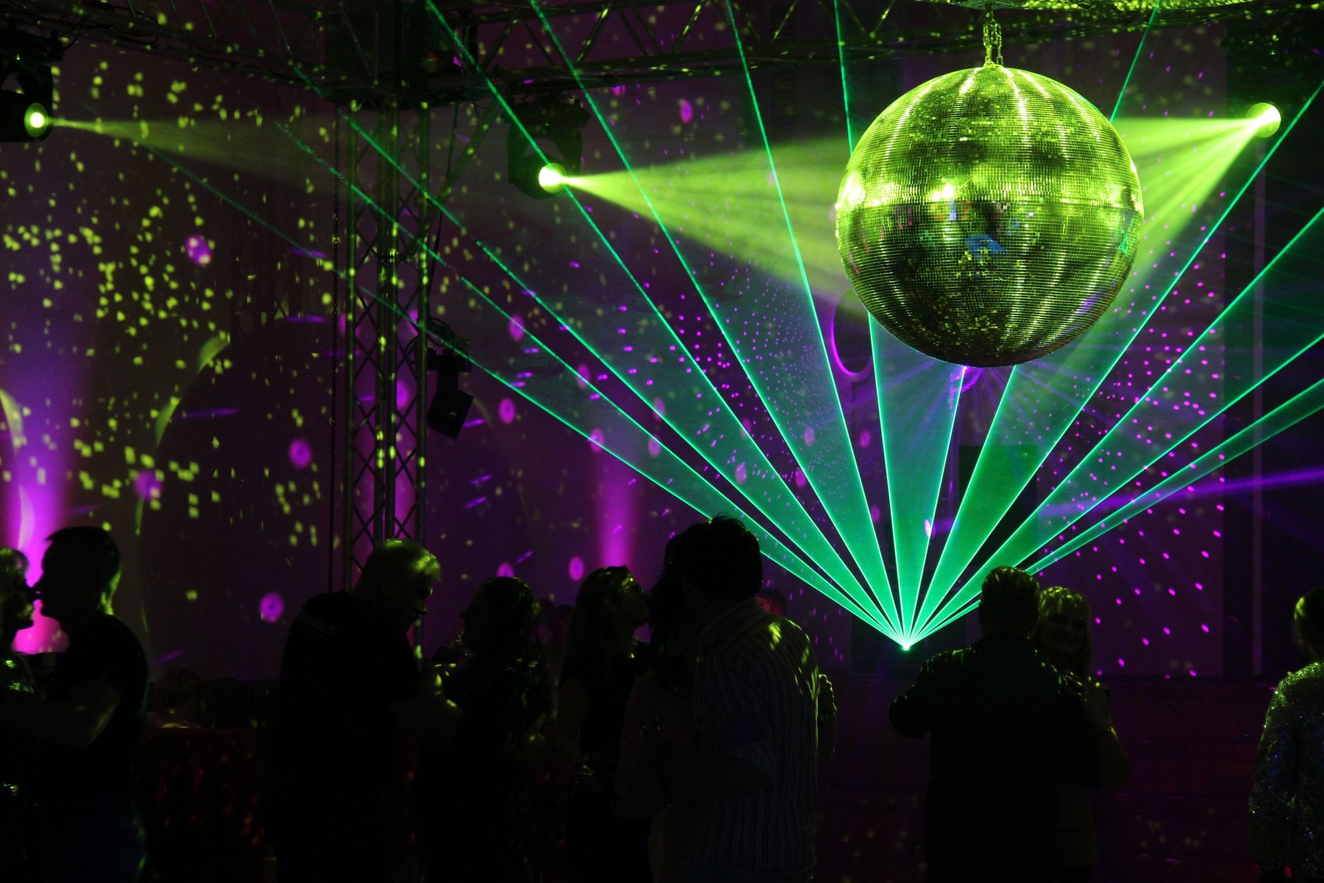 Siluetas de multitud en una discoteca con luces láser verdes y una bola de discoteca.
