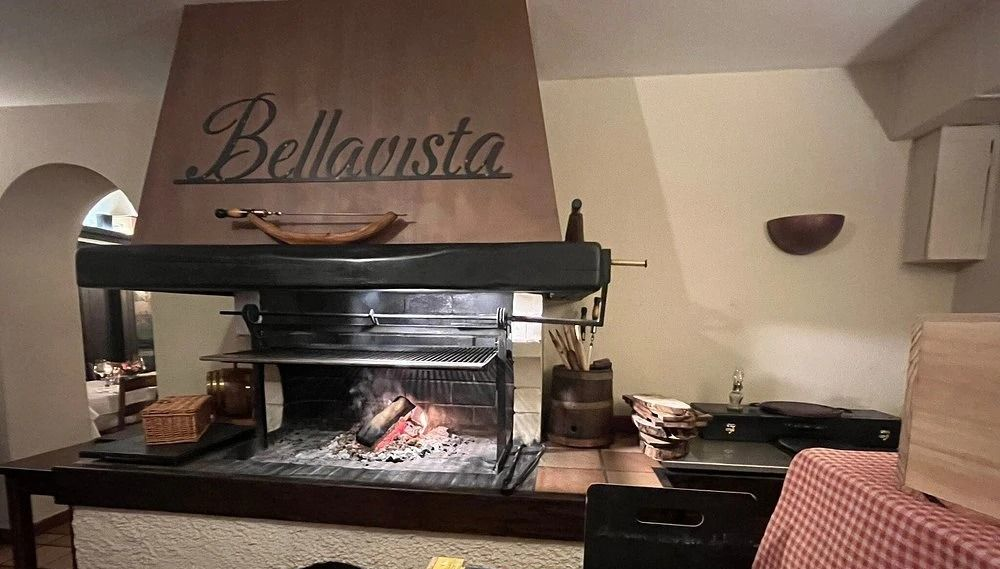 Tagliere di salumi e bicchieri da vino su un tavolo di legno, con vista panoramica sull'esterno.