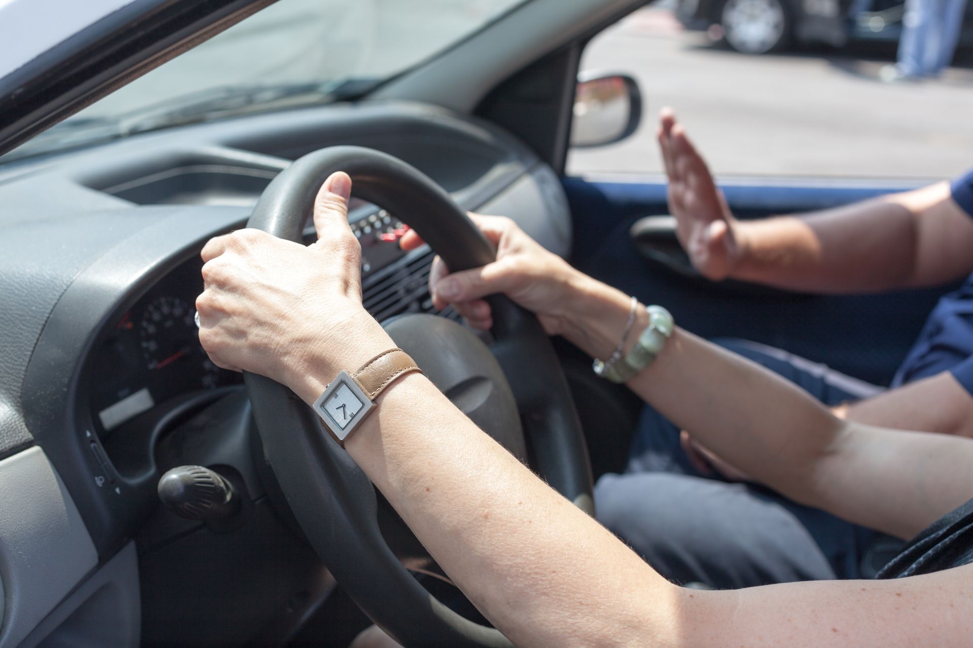 Der Fahrer unterweist einen Beifahrer im Auto, wobei er eine Hand am Lenkrad hat und der Beifahrer neben sich gestikuliert.