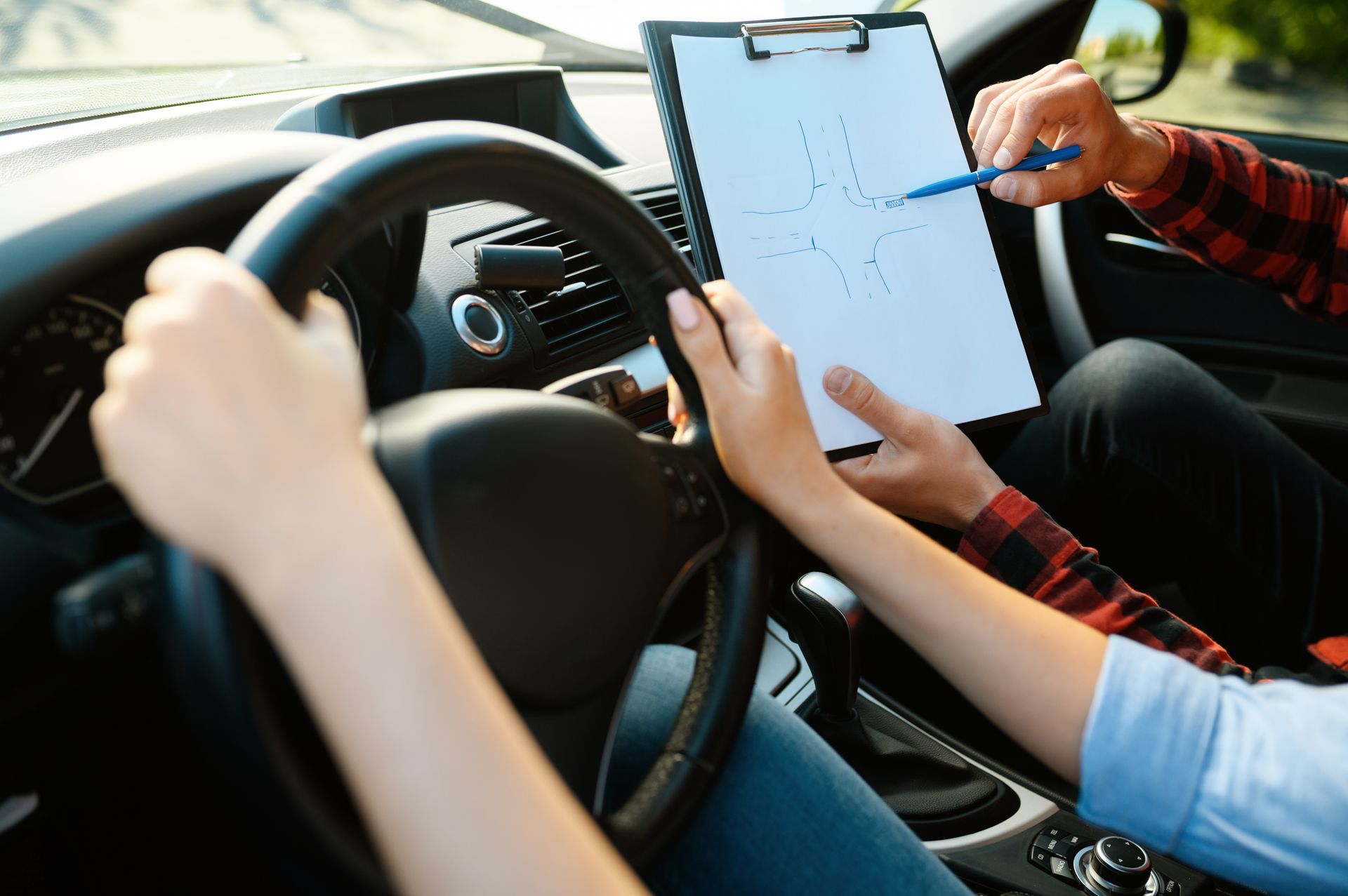 Zwei Personen in einem Auto benutzen ein Klemmbrett mit einer Karte, während sie am Lenkrad sitzen.