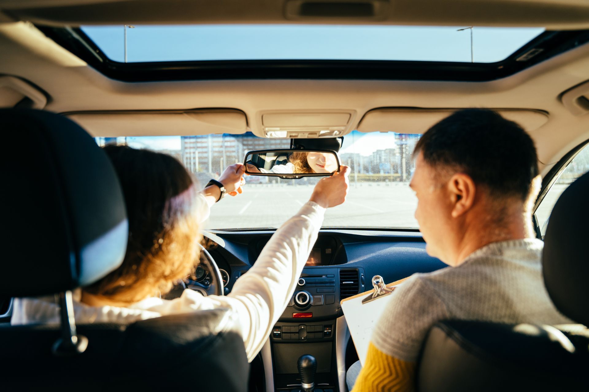 Zwei Personen in einem Auto; eine zeigt in den Rückspiegel, während die andere fährt.