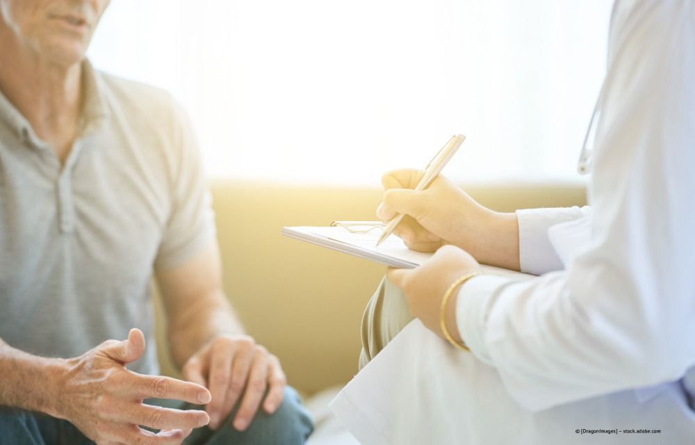 Ein Arzt macht sich während einer Sprechstunde mit einem sitzenden Patienten in einem hellen Büro Notizen.