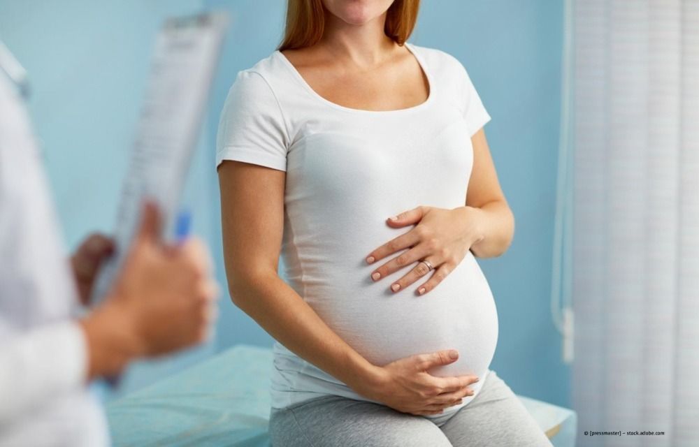 Schwangere Frau in einem weißen Hemd hält sich während einer ärztlichen Untersuchung sanft den Bauch.