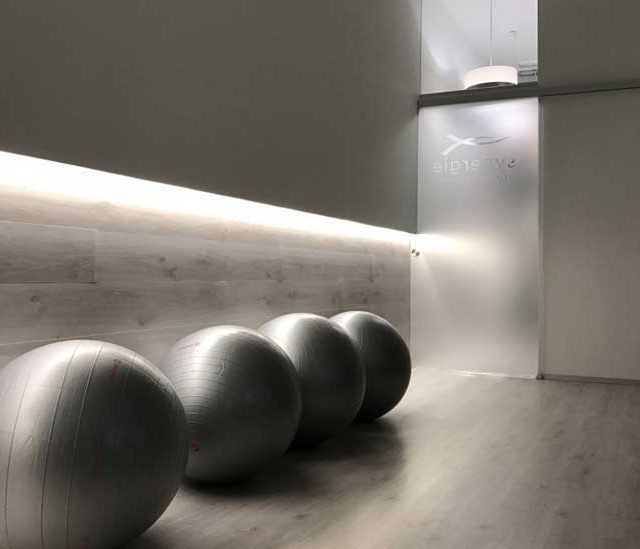 Habitación moderna minimalista con cuatro grandes pelotas de ejercicio grises a lo largo de un pasillo iluminado.