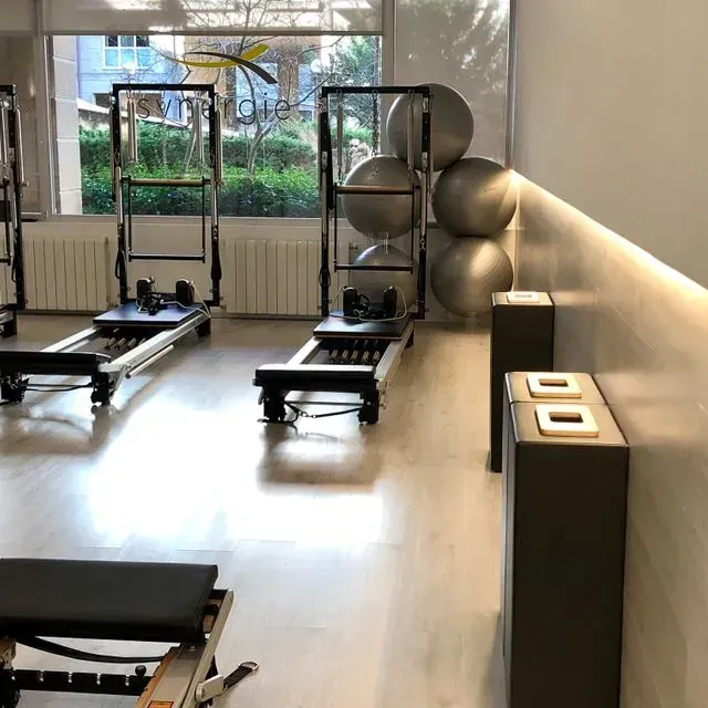 Estudio de Pilates moderno con máquinas reformer, balones de ejercicio y grandes ventanales.