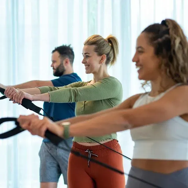 Personas en una clase de fitness haciendo ejercicios con bandas de resistencia en un estudio luminoso.