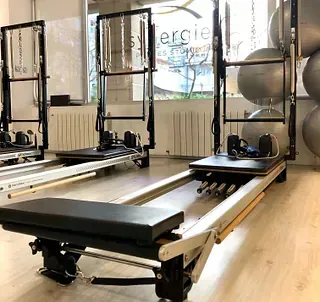 Máquinas de Pilates reformer en un estudio luminoso con espejos y ventanas.