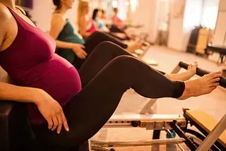 Mujer embarazada usando una máquina de Pilates en un estudio luminoso.