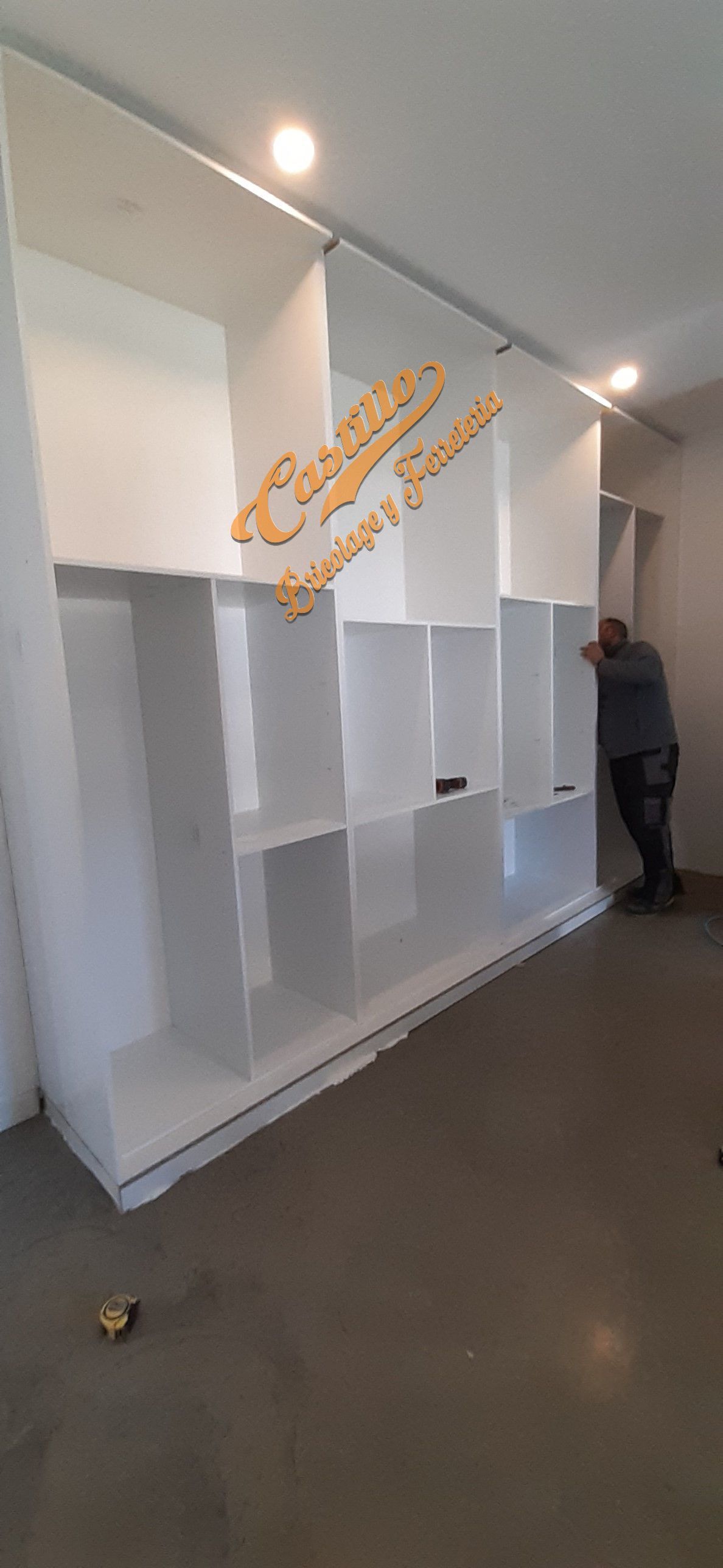 Un hombre está parado frente a una pared de estantes blancos.