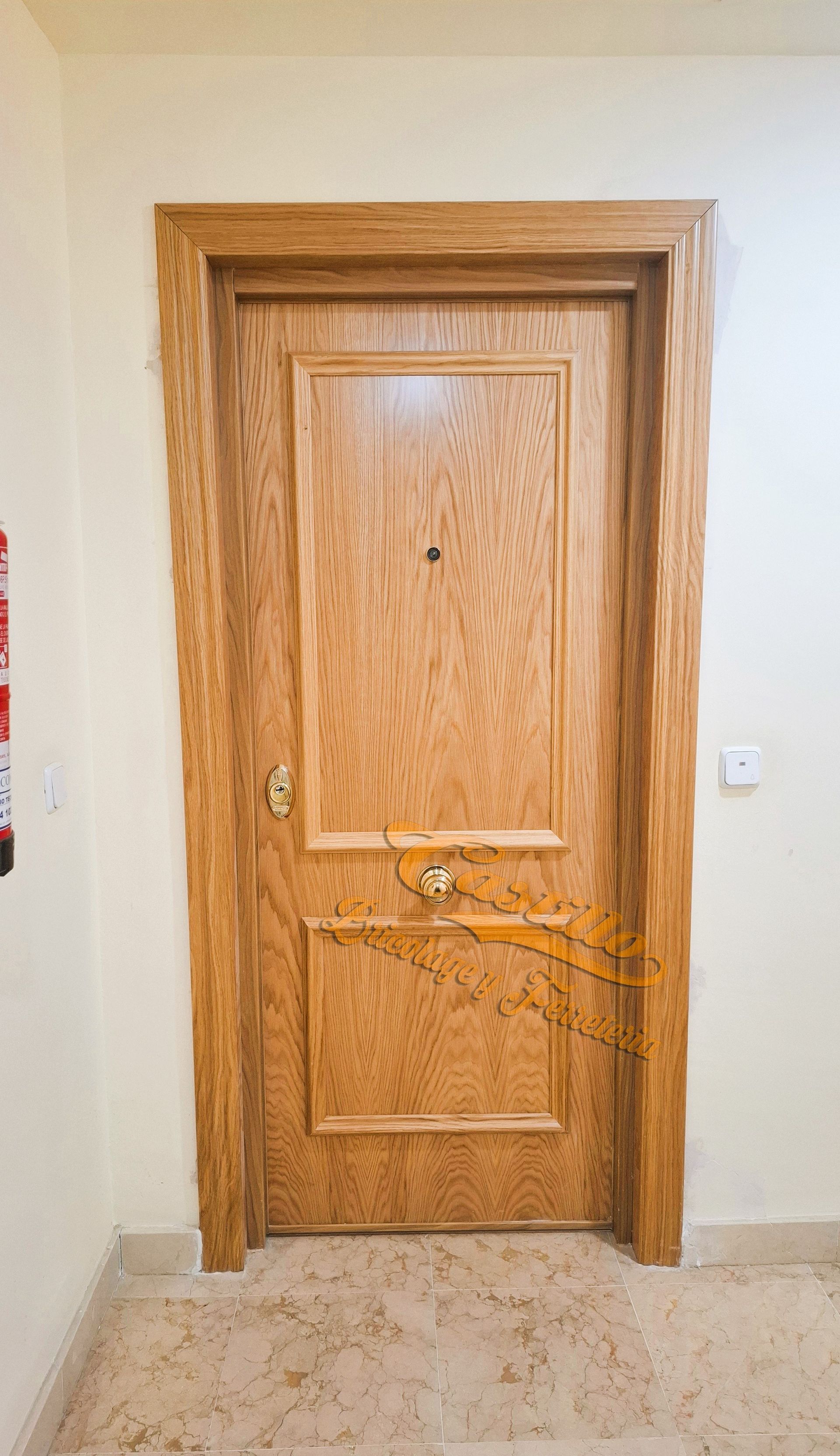 Puerta de madera con herrajes dorados en un pasillo de color beige claro.