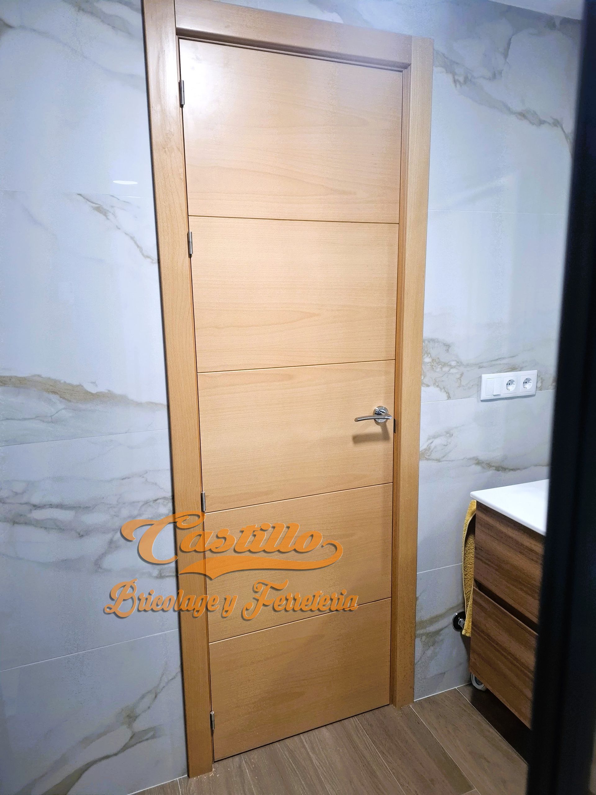 Puerta de madera clara con ranuras horizontales en baño con azulejos efecto mármol.