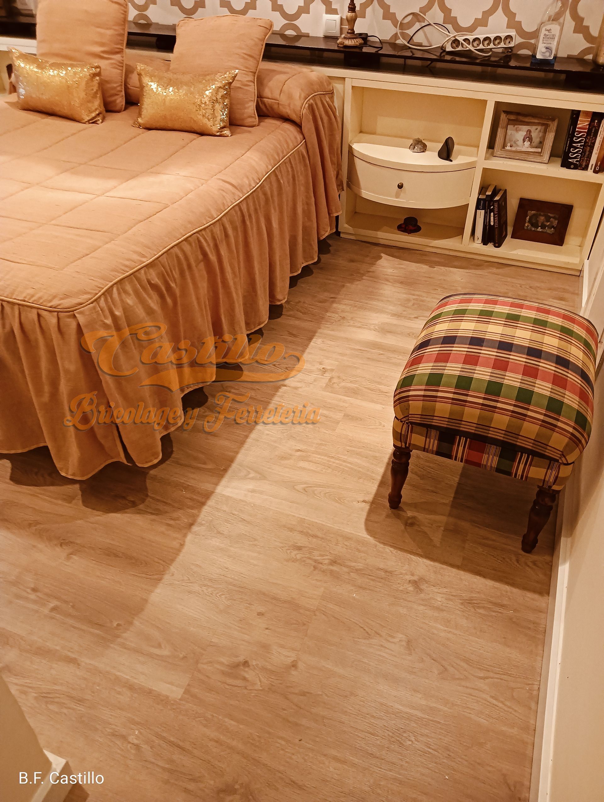 Un dormitorio con cama, otomana, mesita de noche y estanterías.