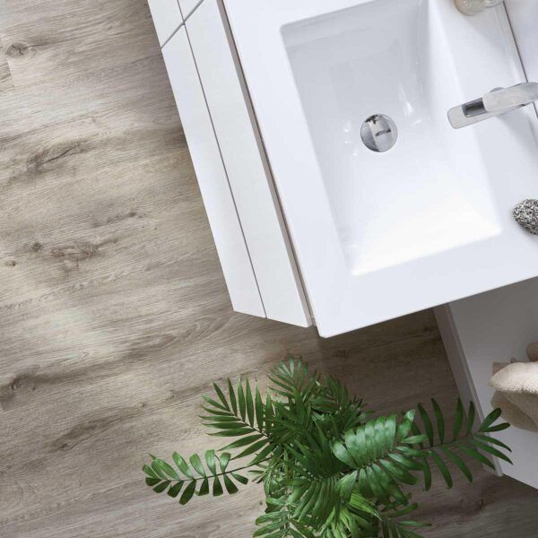 Baño con lavabo blanco, suelo de madera y planta verde.