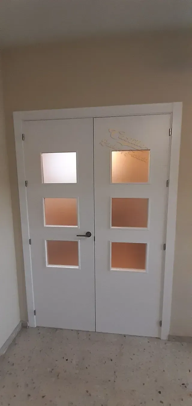 Un par de puertas blancas con ventanas cuadradas en una habitación.