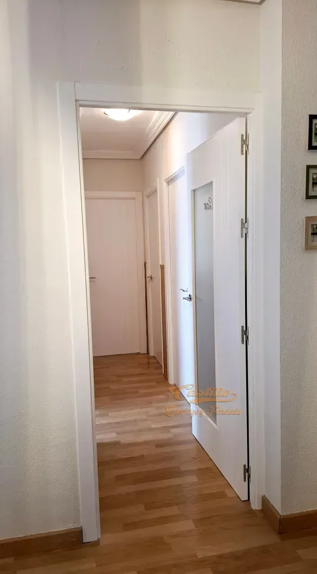 Un pasillo con pisos de madera y puertas blancas que conducen a un dormitorio.