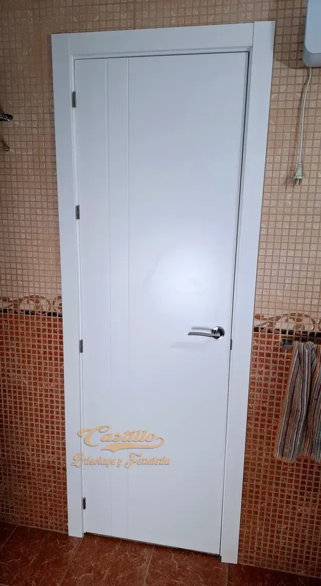 Una puerta blanca está en un baño al lado de una pared de ladrillos.