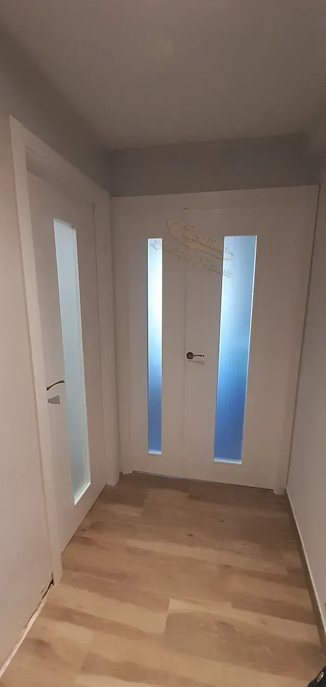 Un pasillo con puertas blancas y suelo de madera.