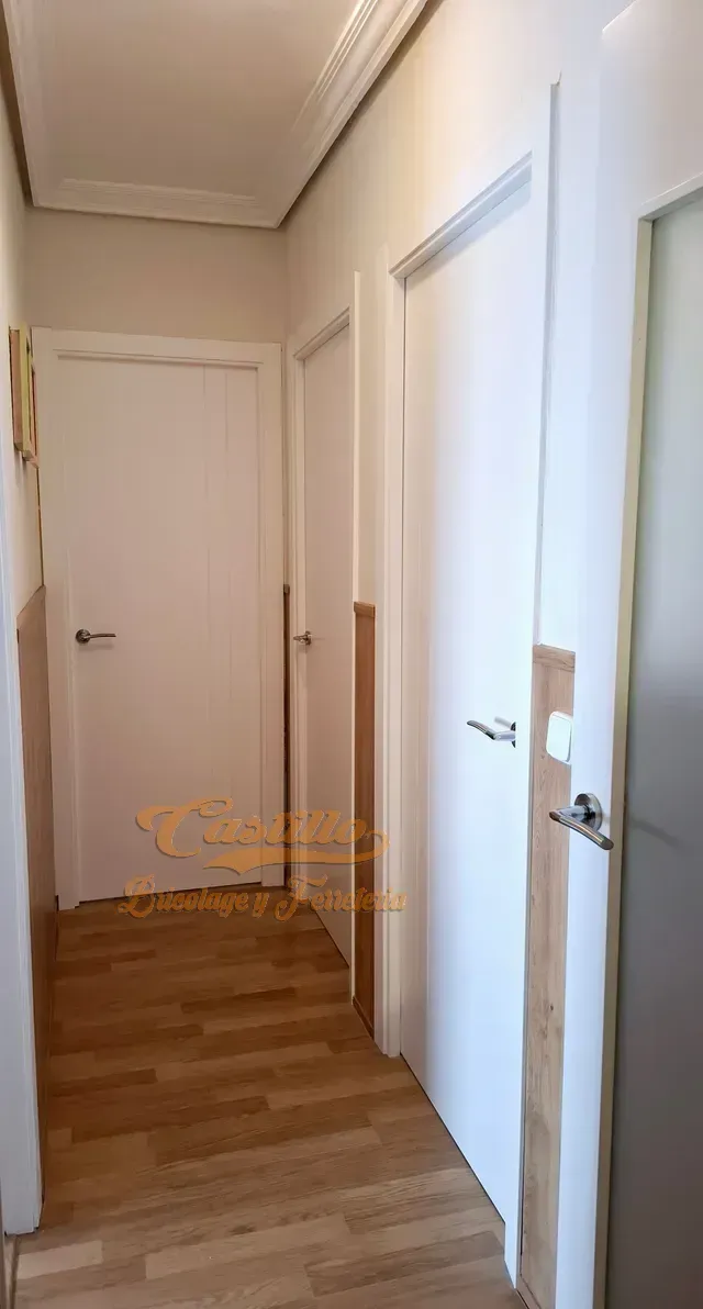 Un pasillo con puertas blancas y suelos de madera.
