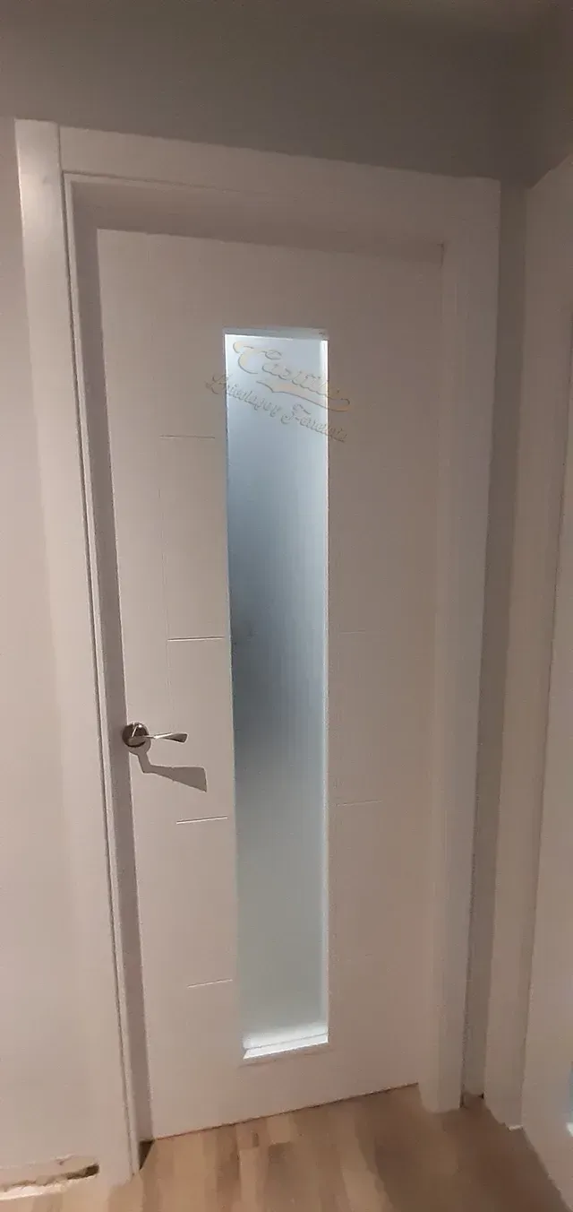 Una puerta blanca con una ventana de vidrio esmerilado en un pasillo.
