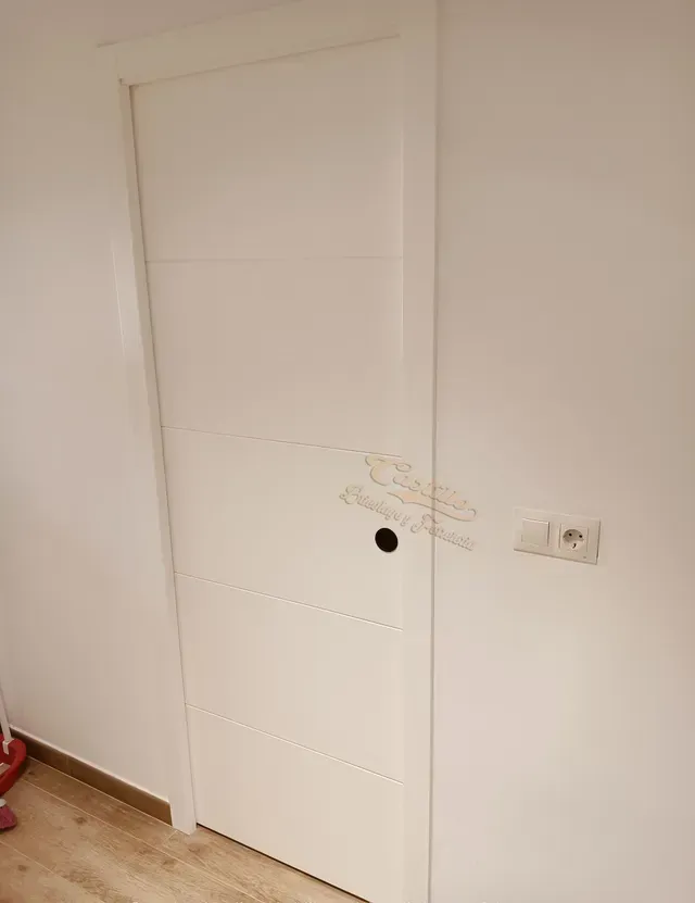 Una puerta blanca está en una habitación al lado de una pared.