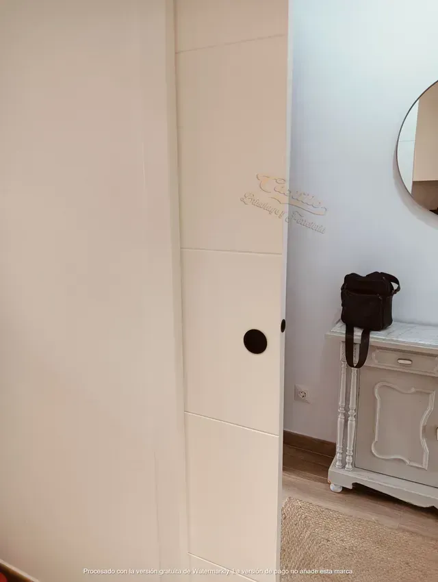 Una puerta blanca se abre a una habitación con un espejo y una cómoda.
