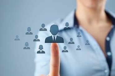 O dedo de uma mulher apontando para um grupo de figuras em silhueta, sugerindo seleção ou gestão.